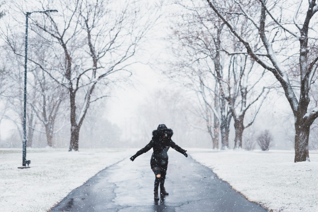 woman wearing black parka jacket standing on road near tall trees and light post during daytime. Photo by Aaron Lee via Unsplash.