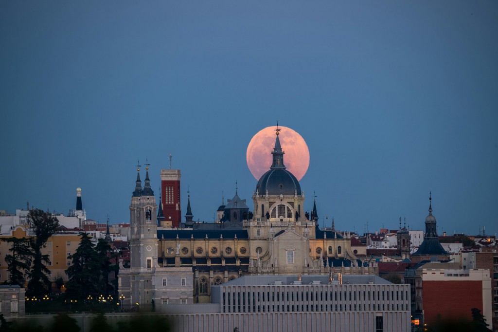 A full moon rises over a city skyline. Photo by Emilio Garcia.