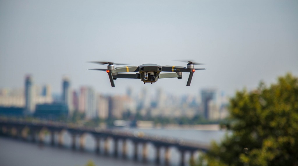 Hovering camera drone with a city in the background.