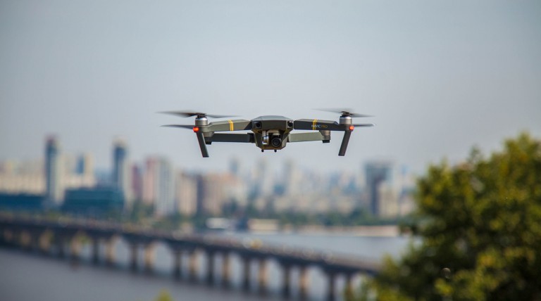 Hovering camera drone with a city in the background.